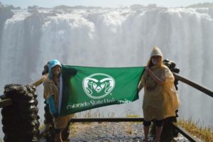 Two CSU students hold a CSU flag in front of a large waterfall