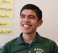 Latino male student with green Rams shirt in front of whiteboard