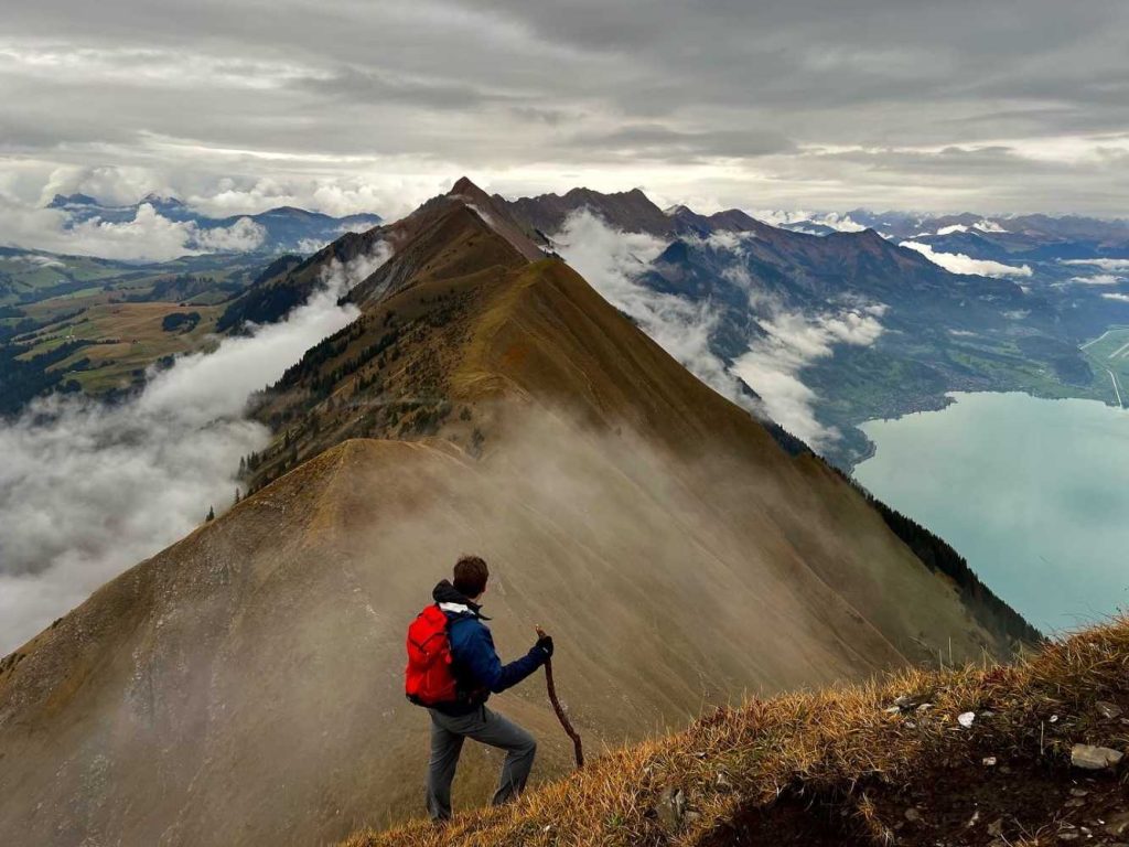 A student backpacking up a mountain with hiker's poles, a mountain peak in the distance