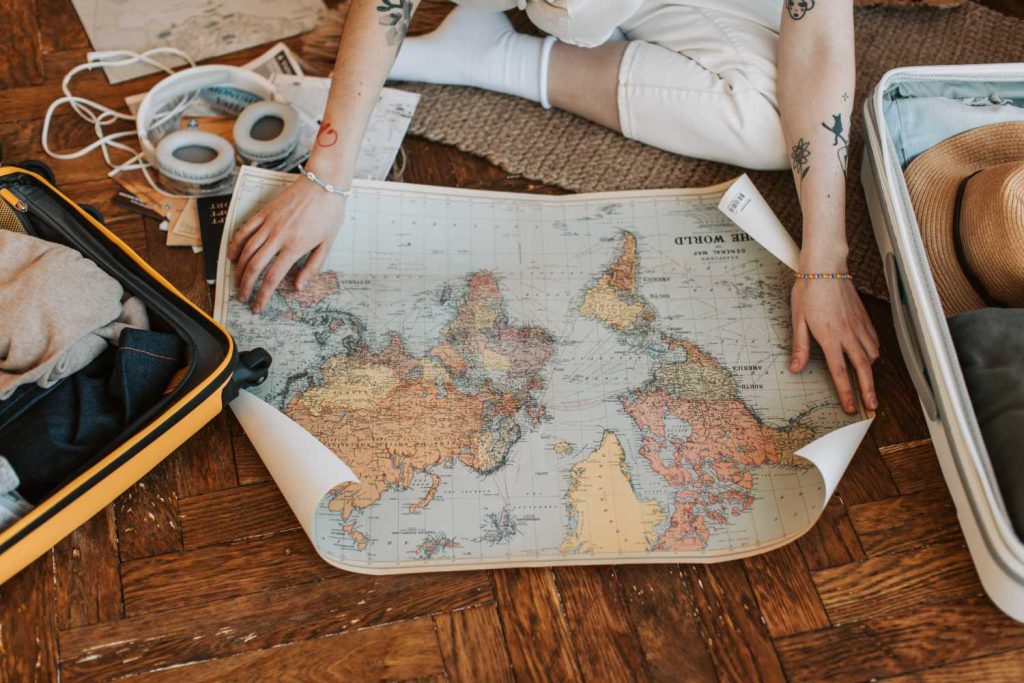 a woman on the ground opens a map of the world next to her suitcase
