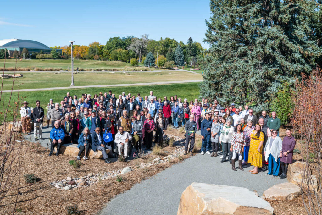 A group of around 100 people stand outside in a circular path on the newly installed garden.