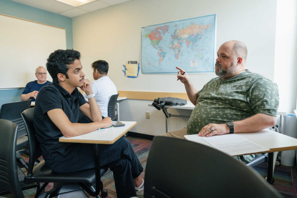 A student and instructor engaged in dialogue. Map in background.