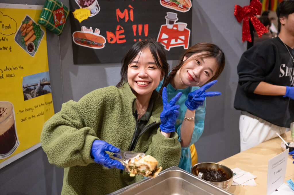Two girls giving the 'peace sign' with their hands while serving food