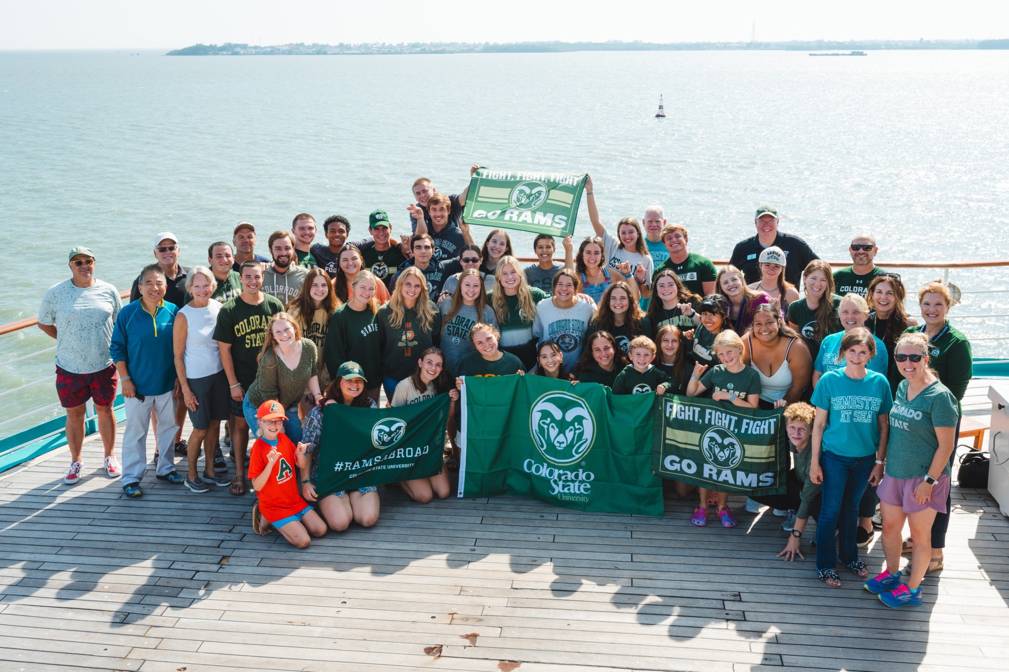 A large group of students dressed in CSU green clothing posing at on a ship at sea.