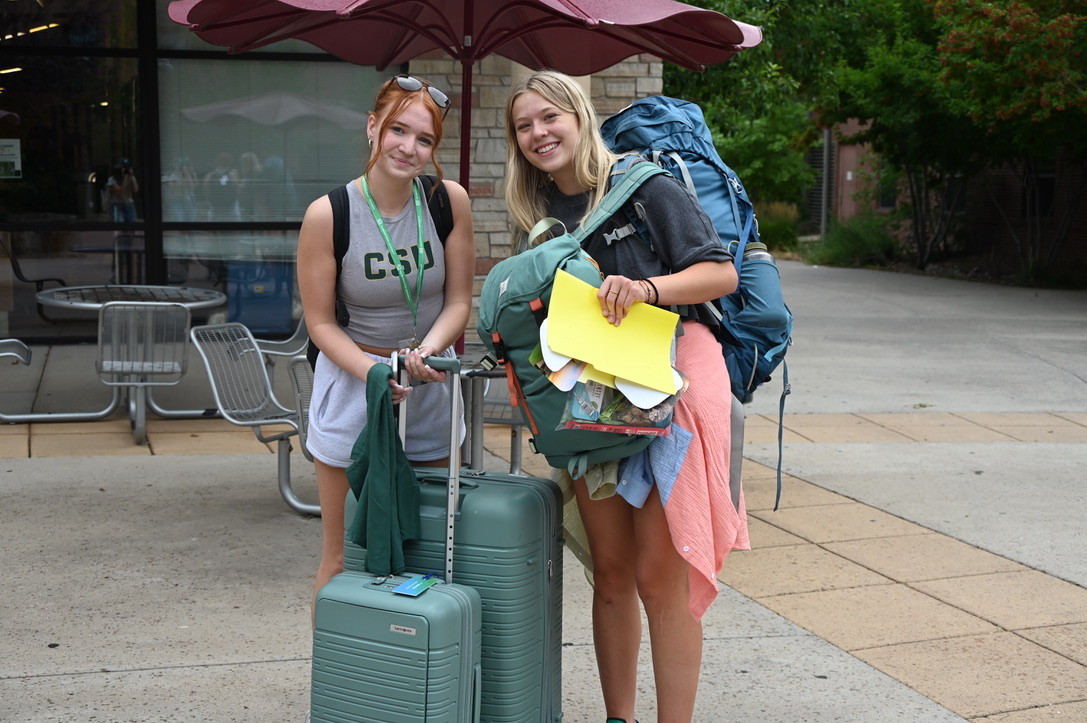 Two students standing with their luggage outside of CSU building