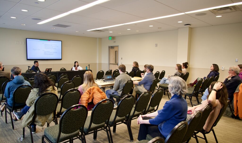 A group of people in a classroom looking at a presentation happening in the front of the room.