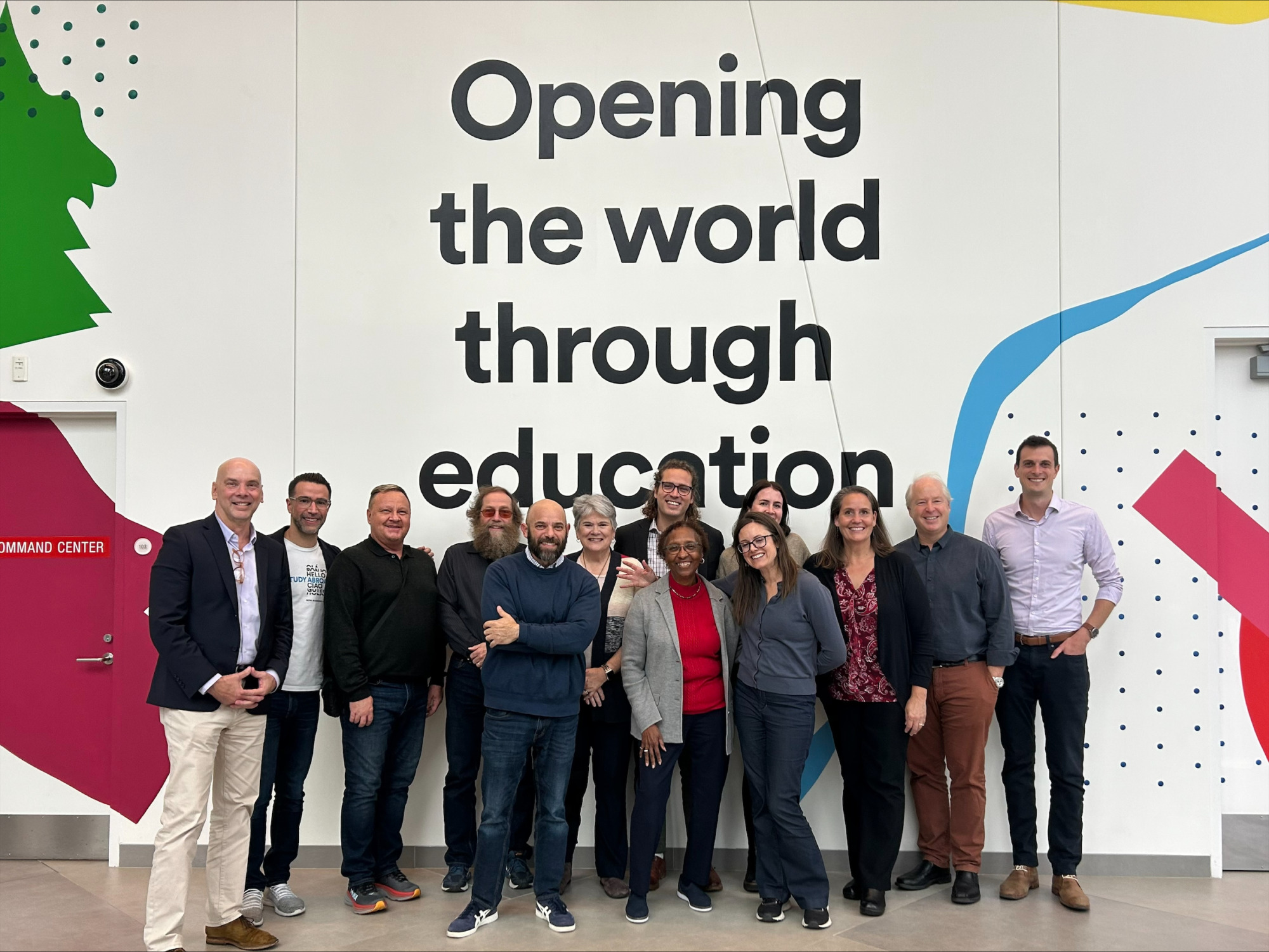 A group of people smiling in front of a wall that reads 'opening the world through education.'