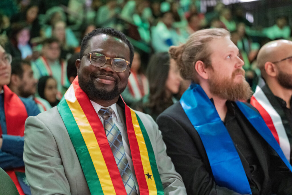 A man wearing a stole from his home country smiling at the camera at graduation