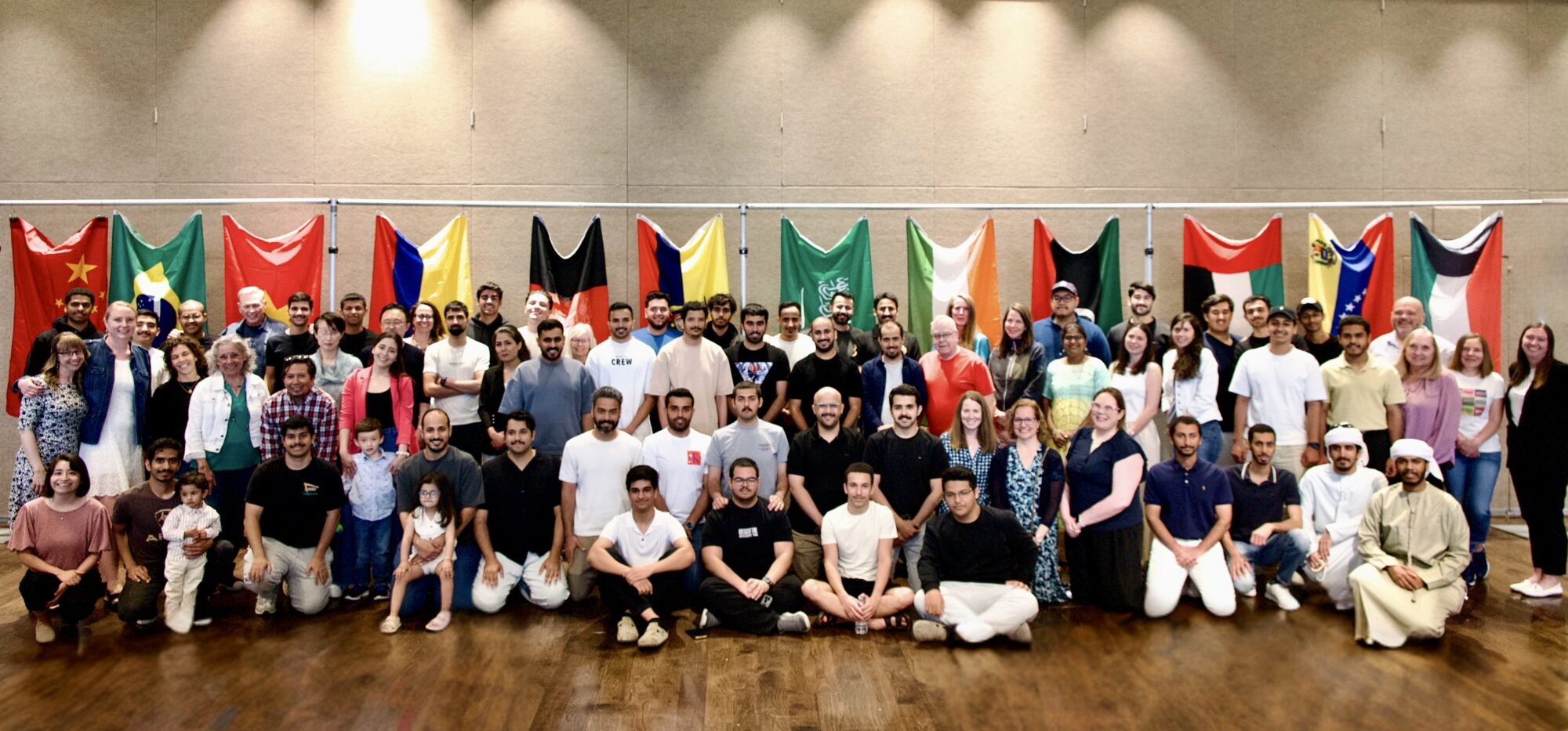 Group photograph of students and staff in the PLACE Intensive English Program. In the background are various flags from different countries.