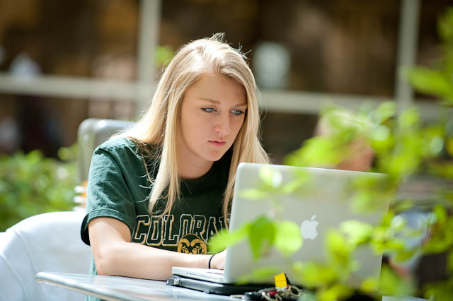 A student wearing a green colorado state t-shirt typing on her computer outside