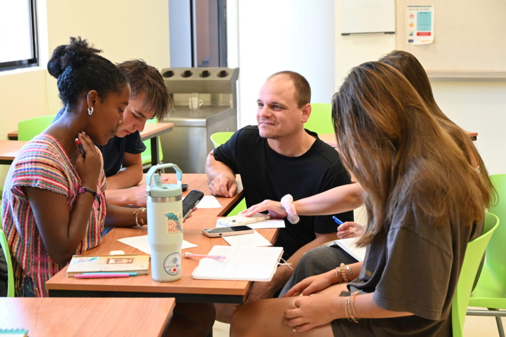 A instructor kneels down to work with a group of students on their group project