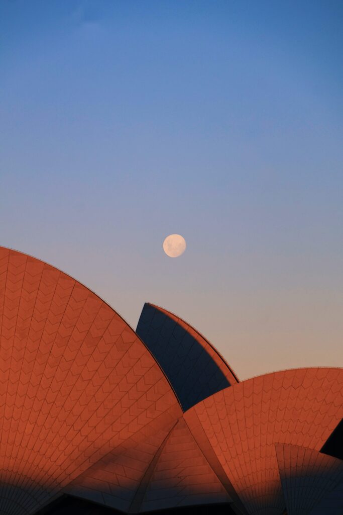A full moon rises over the Sydney opera house at dusk