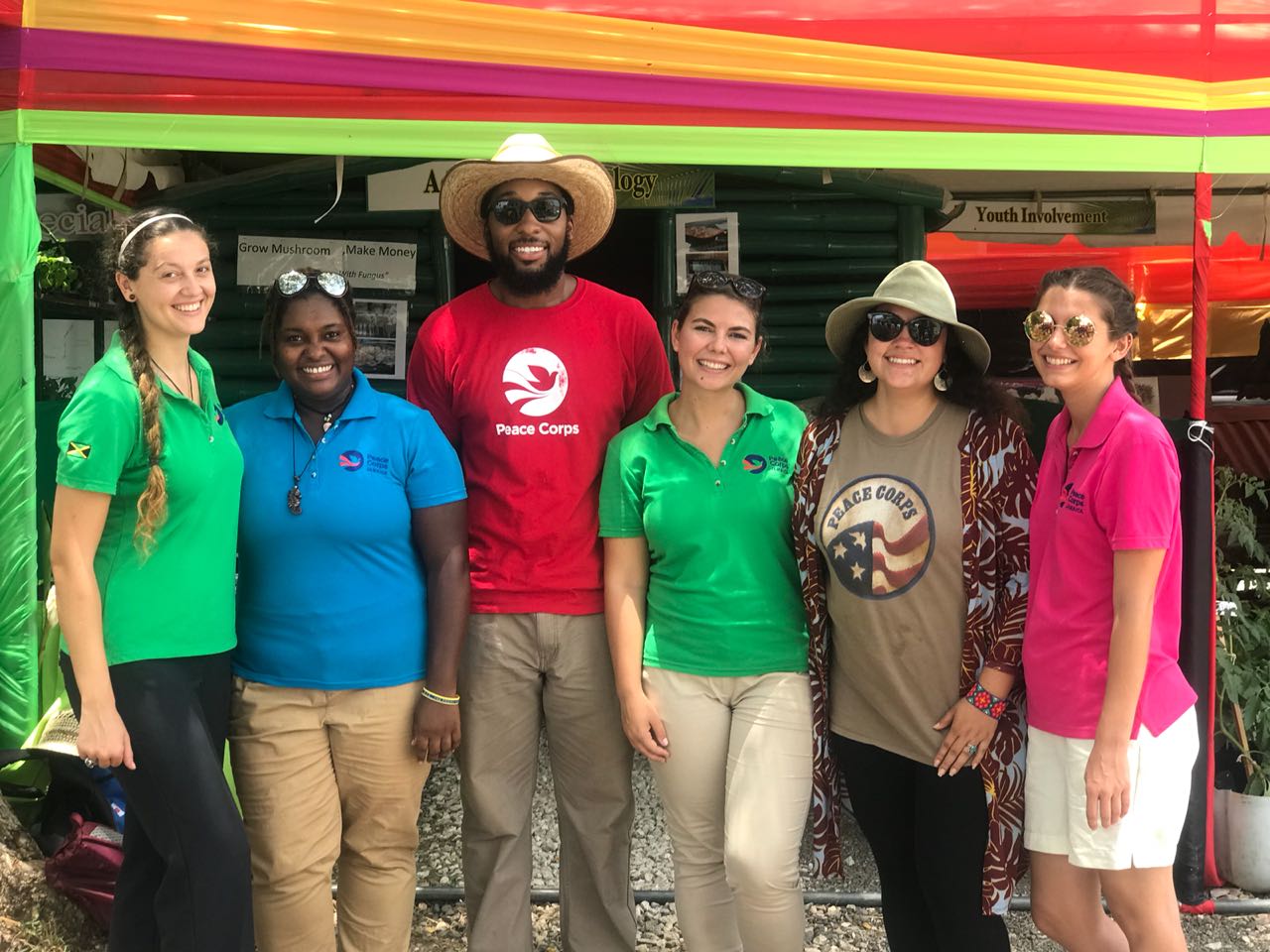 A group of six people stand in a row smiling wearing Peace Corps clothing.