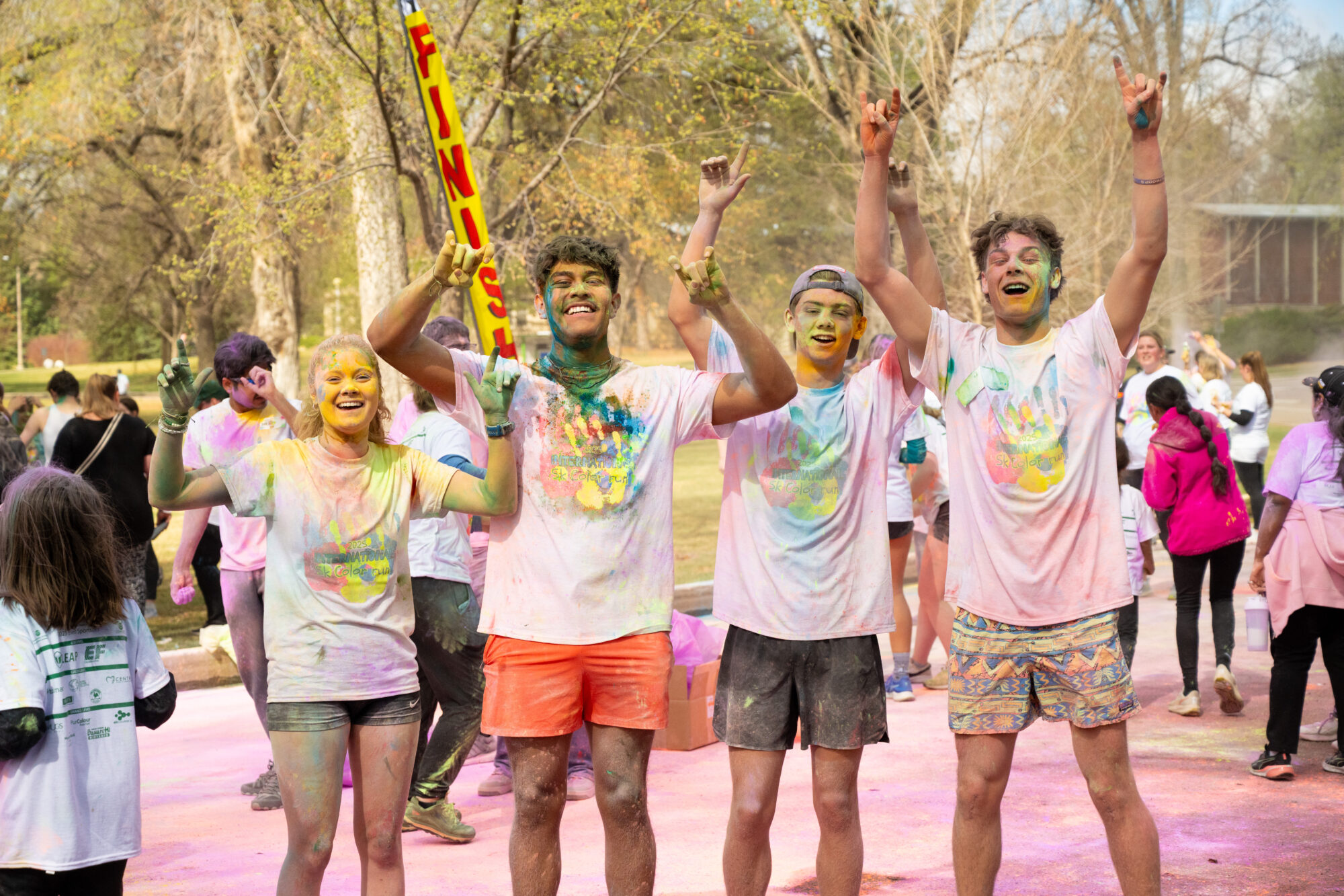 Four people raise their hands in celebration while covered in color powder