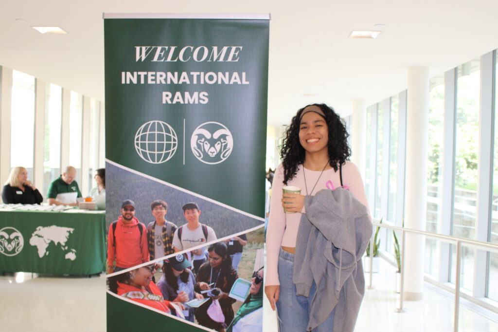A woman smiles next to a sign that says welcome international rams