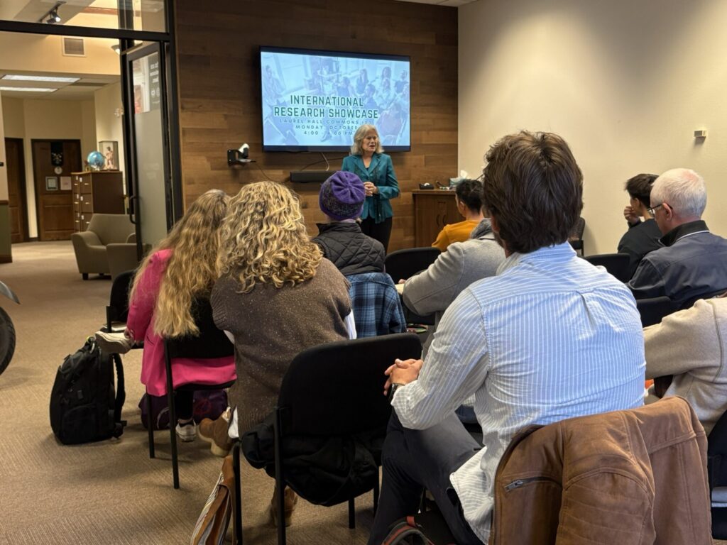 A presenter speaks at the front of the room to a group