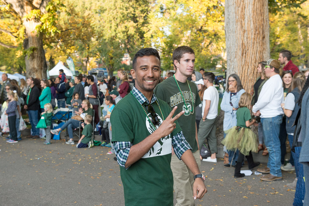 A student wearing a green t-shirt holds up a peace sign while walking in a parade
