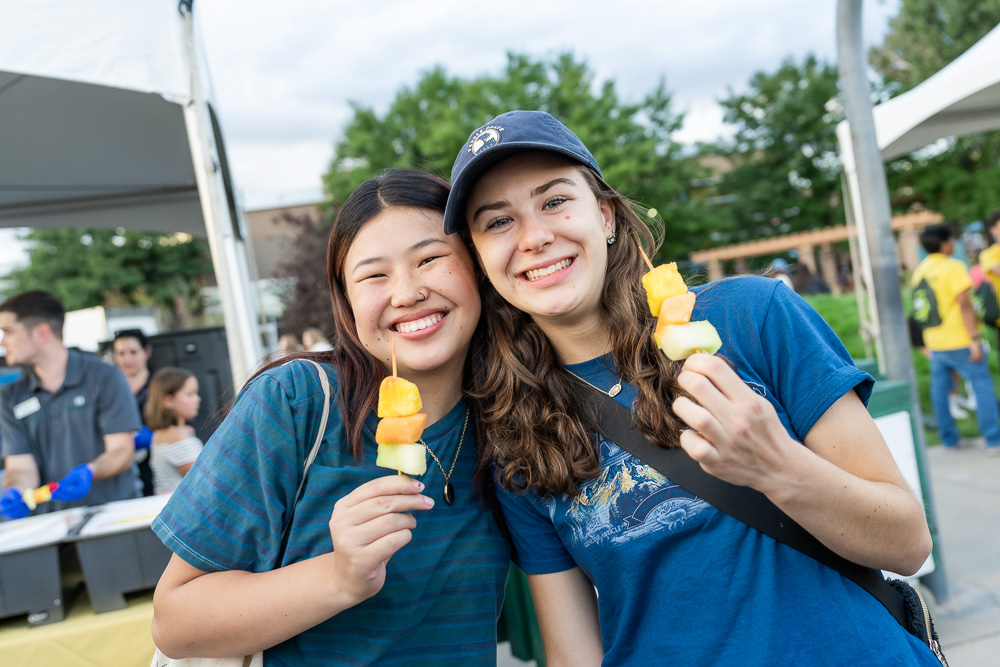 Two students holding up fruit on a stick