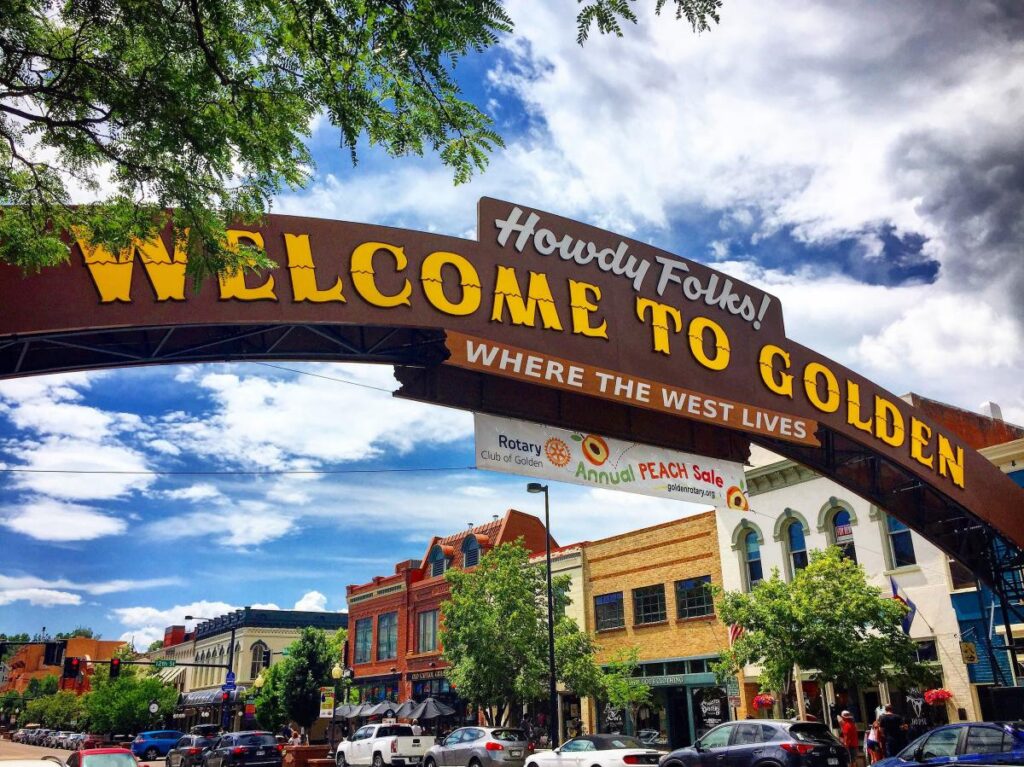 A sign reading “Howdy Folks! Welcome to Golden — Where the West Lives” spans a downtown street
