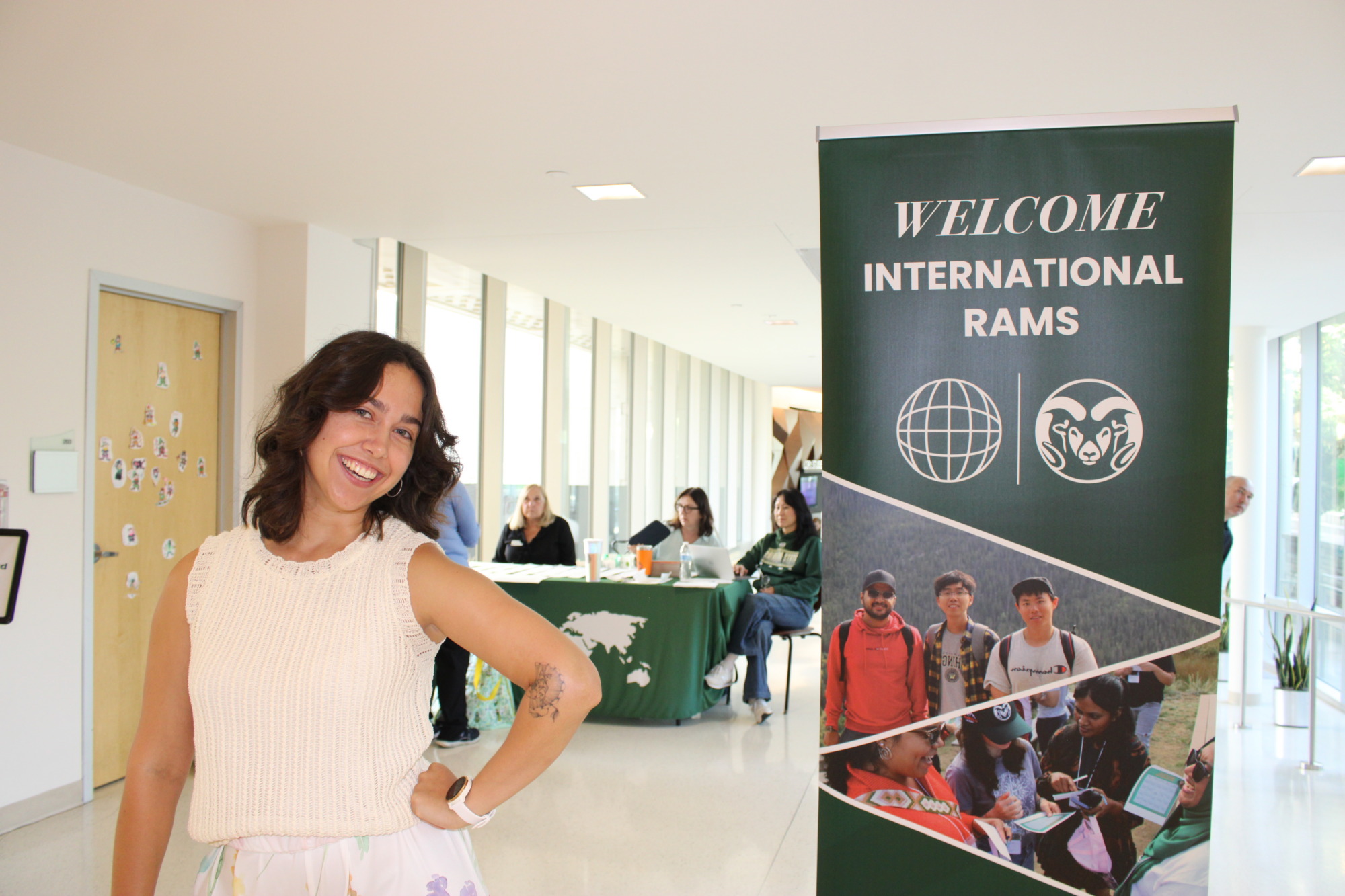 A woman poses next to a sign that reads welcome international rams