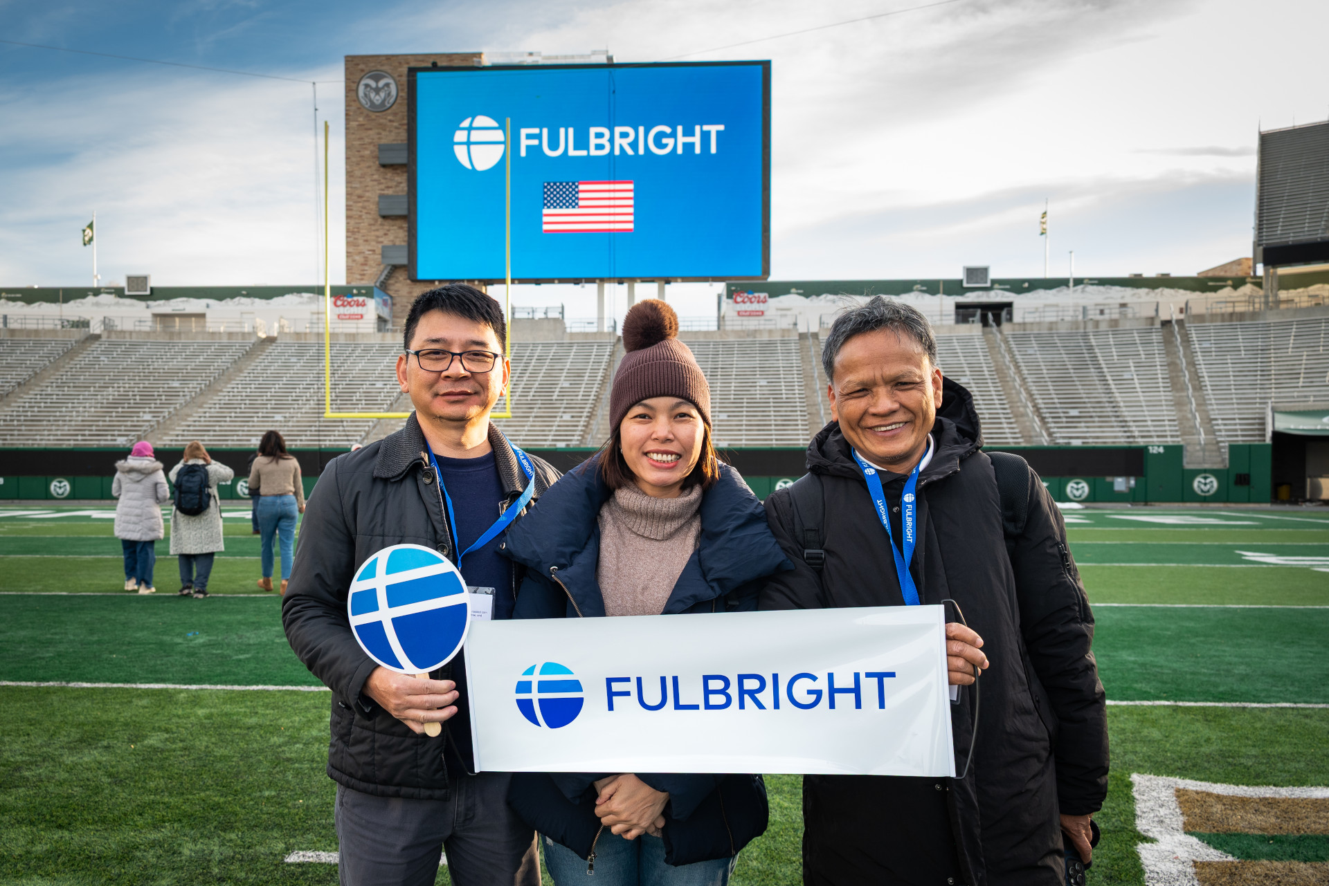 Three scholars stand on the CSU football field holding a Fulbright sign