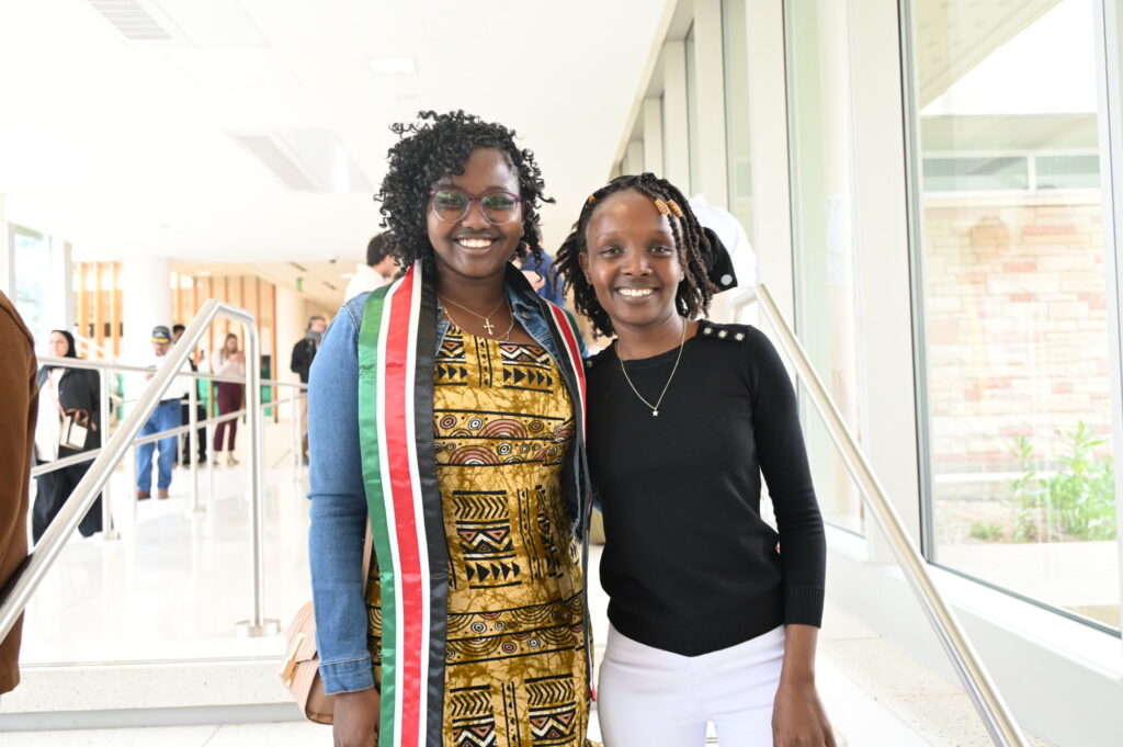 Two students smile for the camera in a hallway