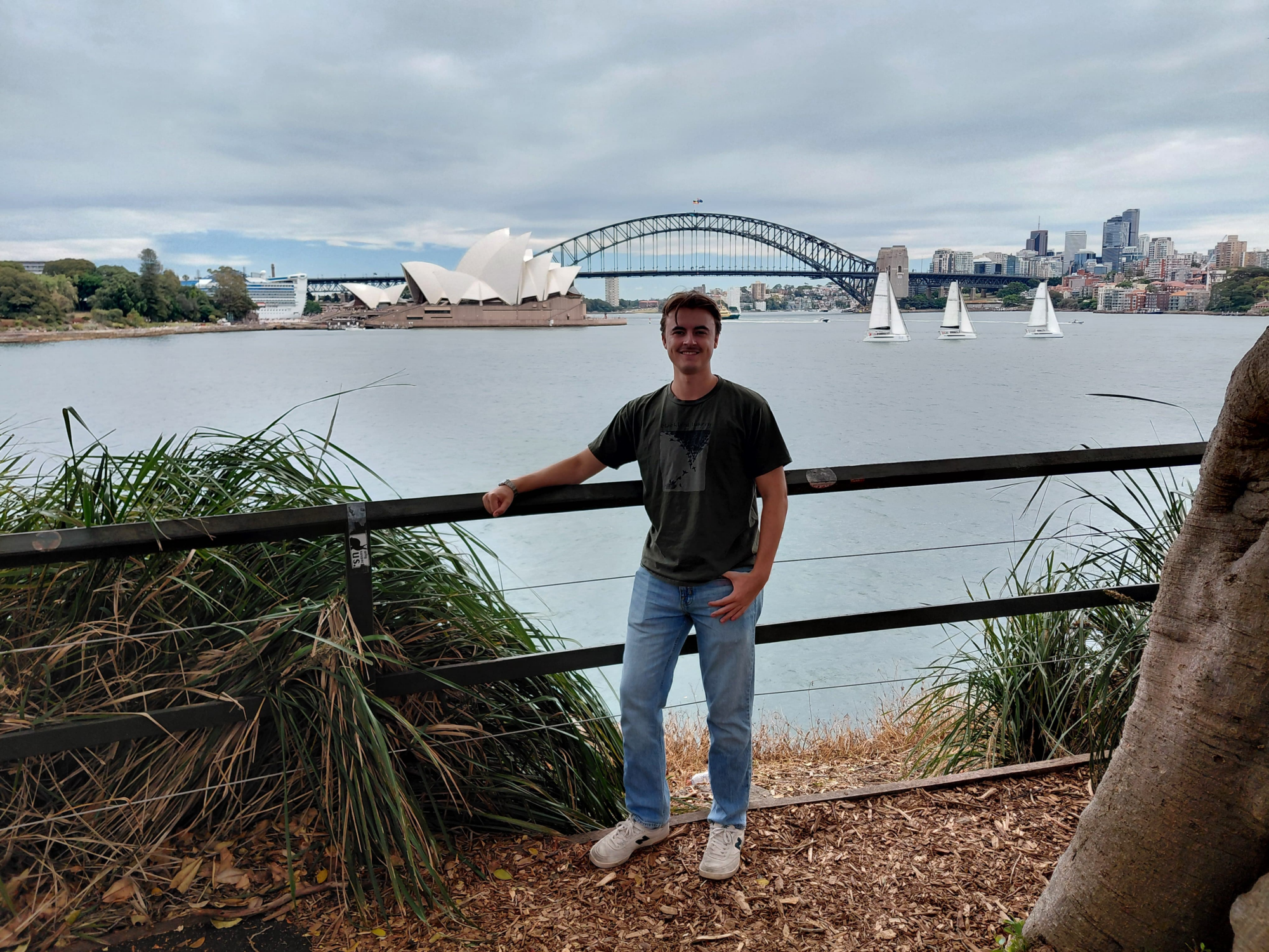 A student stands in front of a body of water with the opera house in the background