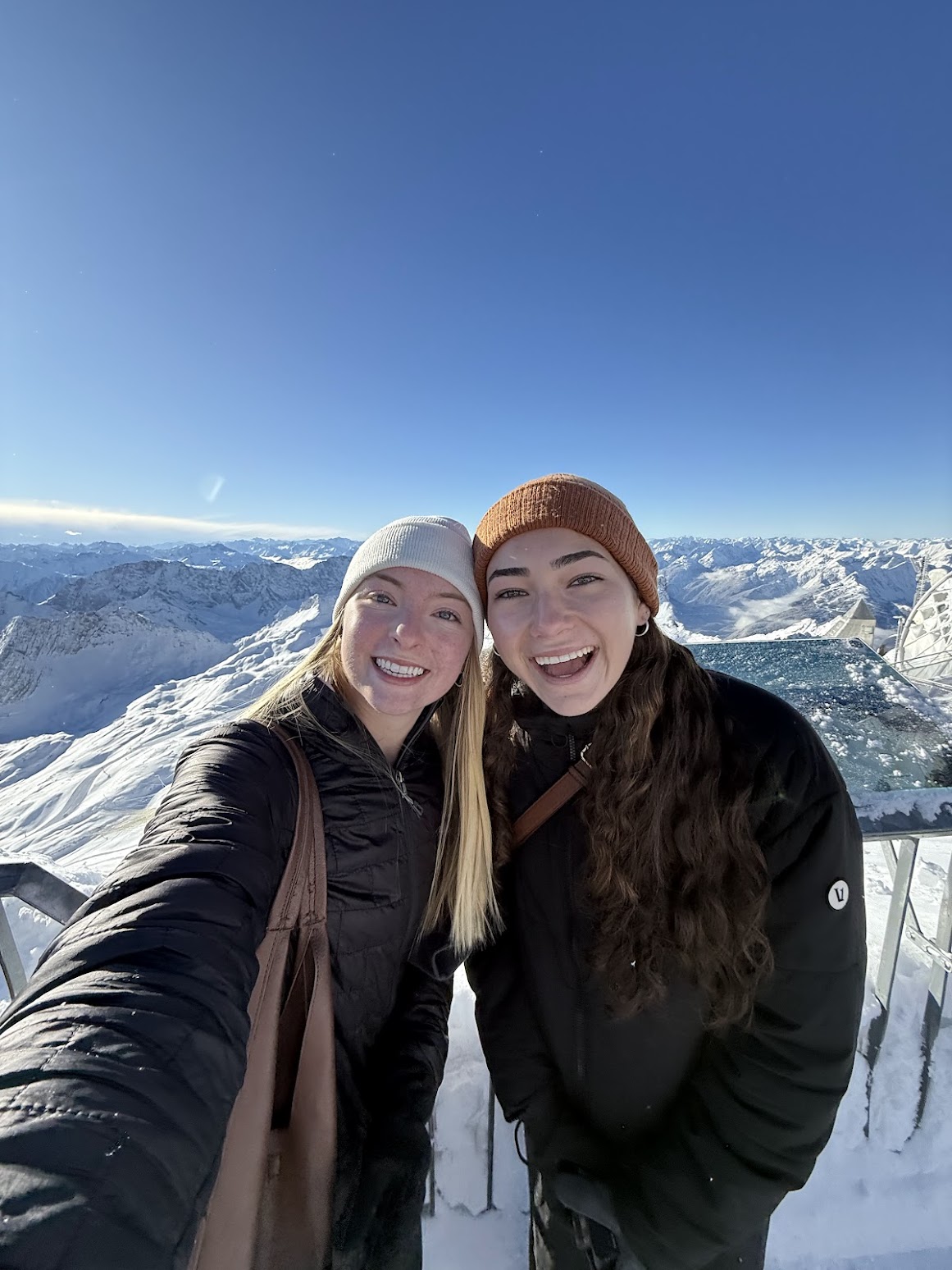 Two gals smile in front of snow covered mountains
