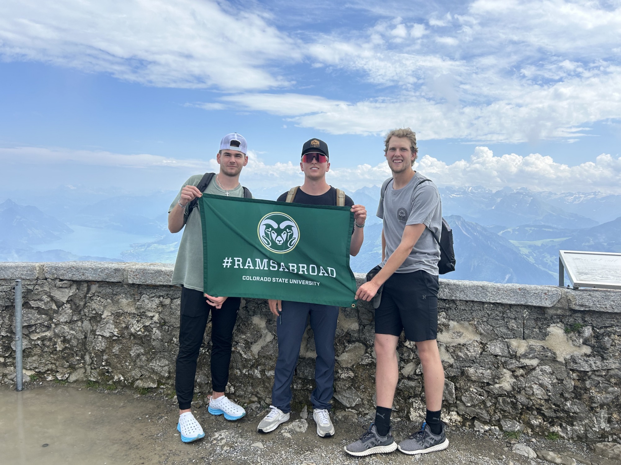 3 students holding a rams abroad flag overlooking a vista