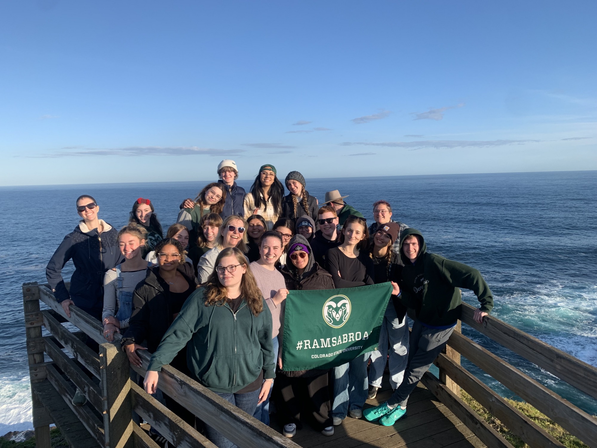 Students holding a ramsabroad flag by the ocean