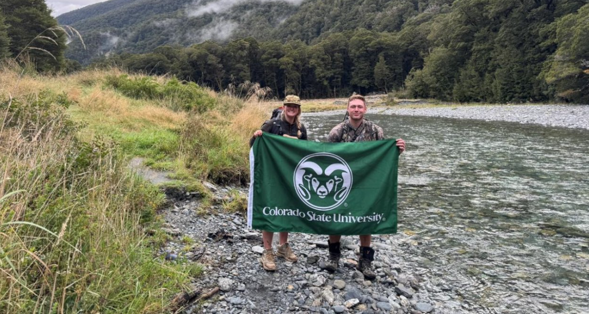 2 students stand in a lake holding a CSU flag