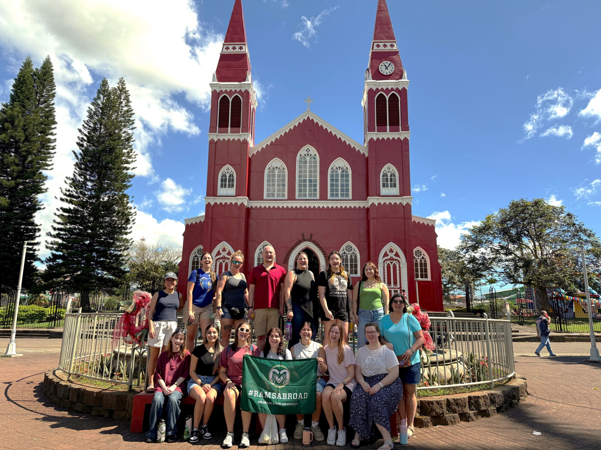 A large group in front of a red cathedral