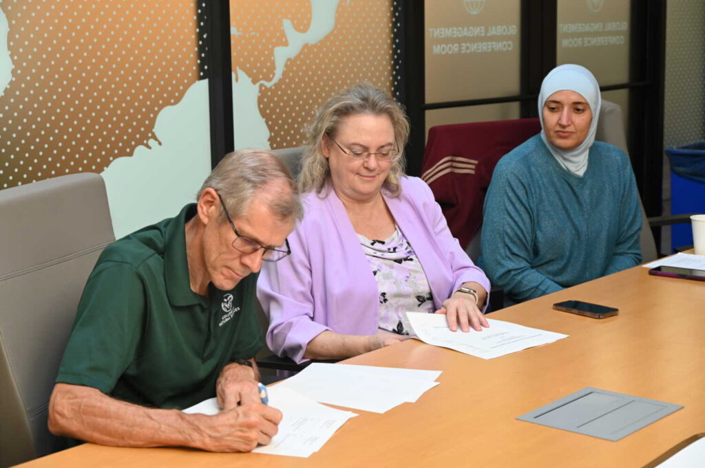Three people sit at a desk signing documents. 